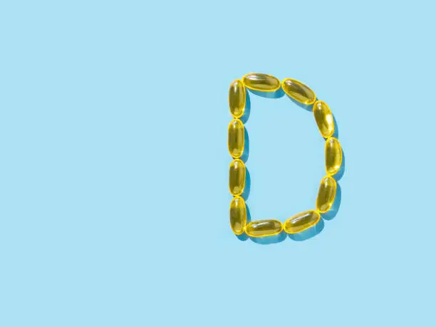 Vitamin D3, Omega or Evening Primrose Oil gel capsules on blue background. Top view or flat lay. Letter D made from yellow liquid capsules with D3 nutritional supplement oil. Copy space left.