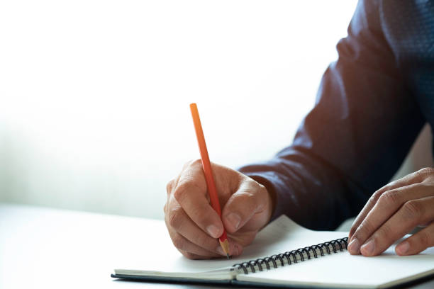 istock Close-up of man hand using writing pencil memo on notebook paper or letter, diary on table desk office. Workplace for student, writer with copy space. business working and learning education concept. 1307571254