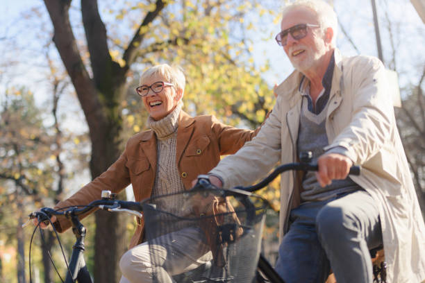 Cheerful active senior couple with bicycle in public park together having fun Cheerful active senior couple with bicycle in public park together having fun. Perfect activities for elderly people. Happy mature couple riding bicycles in park man 60s bicycle stock pictures, royalty-free photos & images