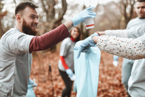 istock Smiling Male Volunteer Putting Disposable Coffee Cup In Bag While Collecting Trash From Forest 1307571742
