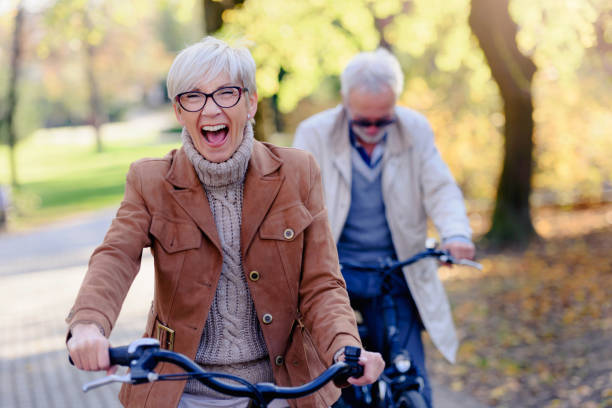 Cheerful active senior couple with bicycle in public park together having fun