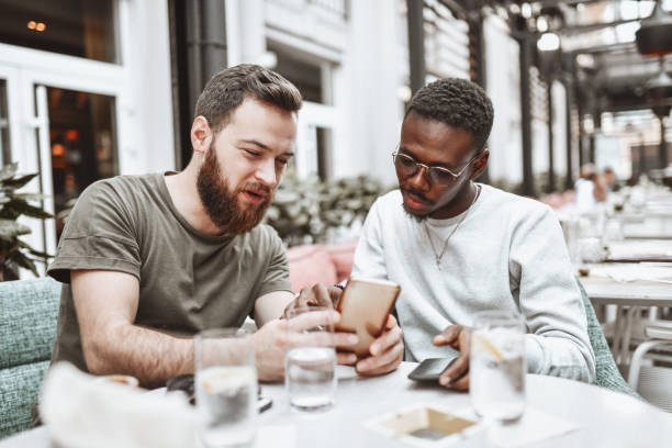 Multiethnic Gay Couple Checking Each Other's Socials While Having Date Together