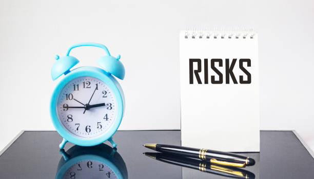 istock Notepad with the text Risks on a black mirrored background and a white background. Pen, alarm clock nearby. business, banking, finance and investment concept 1307577250