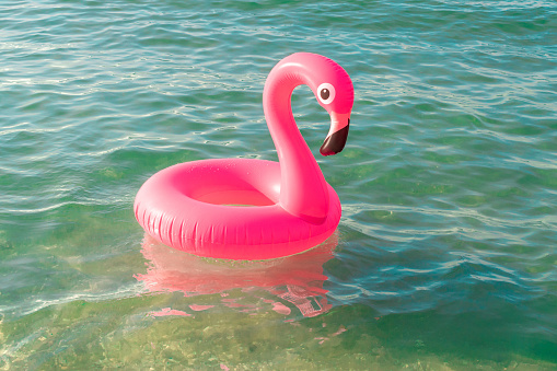 Summer fun beach. Pink inflatable flamingo in blue sea water on summer ocean beach background. Funny bird toy for kids