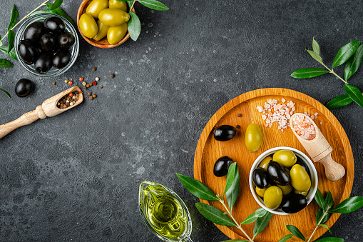 Olive oil and olives with leaves and pink salt on dark background. Overhead, copy space