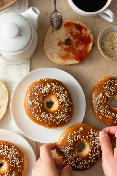 istock Bagels pastry buns for breakfast,with coffee cup and fruit jam. Top view, bright background, natural light. 1307578292