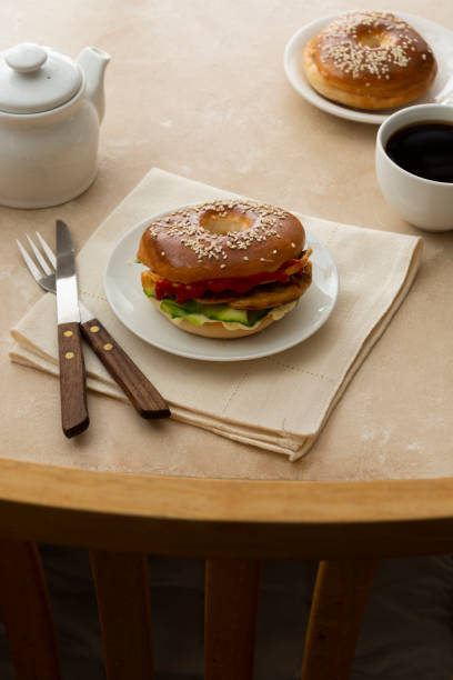 istock Bagels breakfast sandwich with cucumber and eggs, pastry buns, morning coffee cup at table and chair 1307578336