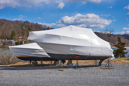 Cold Spring Harbor, NY USA - March 14, 2021: A Boat yard with winter storage of power boats, placed on blocks, and shrink-wrapped to protect them from snow and rain.