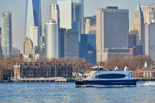 A New York Waterway Ferry in New York Harbor. Behind the Ferry is Governors Island, and in behind that is the Lower Manhattan Skyline New York, NY - March 11 2021: A New York Waterway Ferry in New York Harbor in the late afternoon. Behind the Ferry is Governors Island, and behind that is the Lower Manhattan Skyline liberty tower stock pictures, royalty-free photos & images