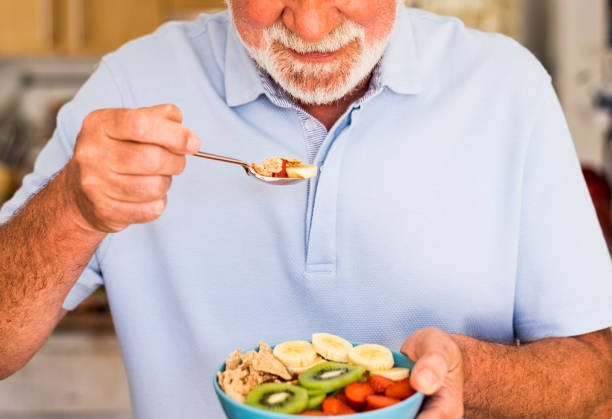 l�ächelnder älterer mann hält eine schüssel mit frischen und getrockneten früchten. frühstück oder mittagessen, gesunde ernährung - ballaststoff stock-fotos und bilder