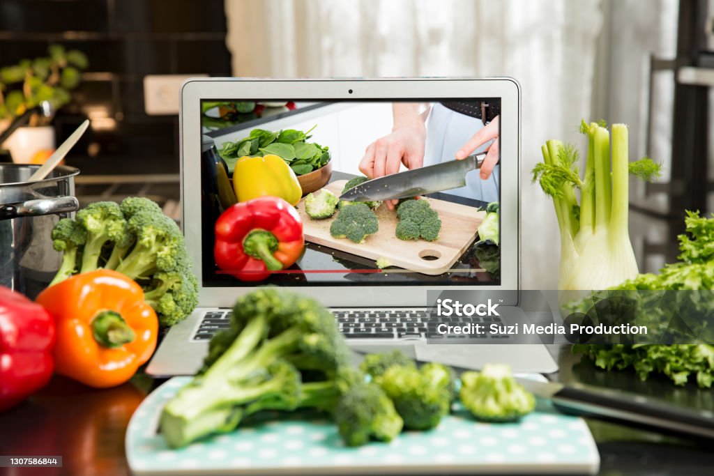 Man watching video recipe on laptop and cooking at home. Beautiful happy woman streaming broadcast video blog about tasty and healthy food from home kitchen. Healthy lifestyle and social media. Man watching video recipe on laptop and cooking at home. Food Stock Photo