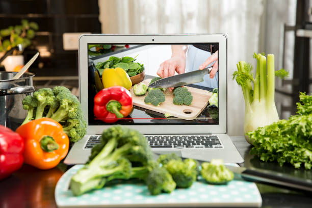 Man watching video recipe on laptop and cooking at home. Beautiful happy woman streaming broadcast video blog about tasty and healthy food from home kitchen. Healthy lifestyle and social media. Man watching video recipe on laptop and cooking at home. cooking show stock pictures, royalty-free photos & images