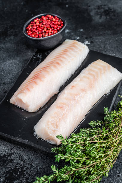 istock Raw cod loin fillet fish on marble board. Black background. Top view 1307594180