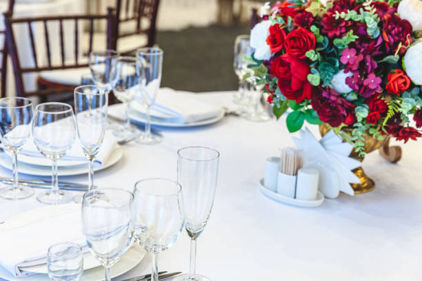istock Fancy table set for dinner with flower composition in restaurant, luxury interior background. Wedding elegant banquet decoration and items for food arranged by catering service on white table 1307594336