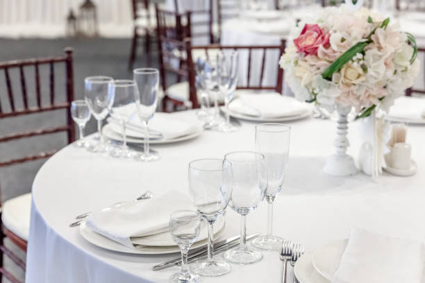 istock Fancy table set for dinner with flower composition in restaurant, luxury interior background. Wedding elegant banquet decoration and items for food arranged by catering service on white table 1307594350