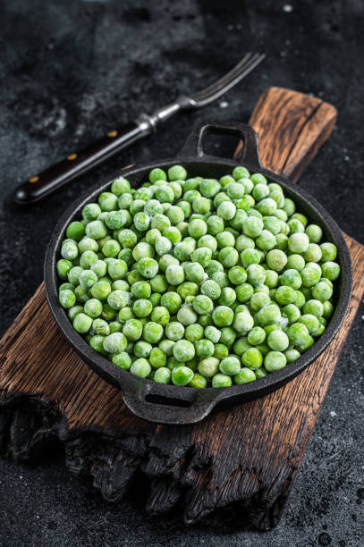 istock Fresh Frozen green peas in a pan. Black background. Top view 1307597171
