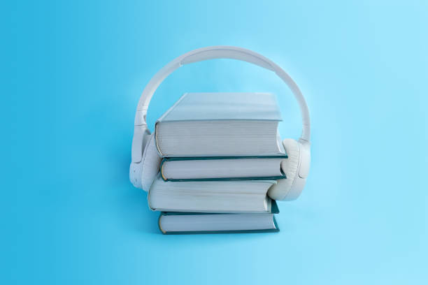 istock Wireless white headphones on stack of books on light blue background. Concept for audiobooks in minimal style 1307598301