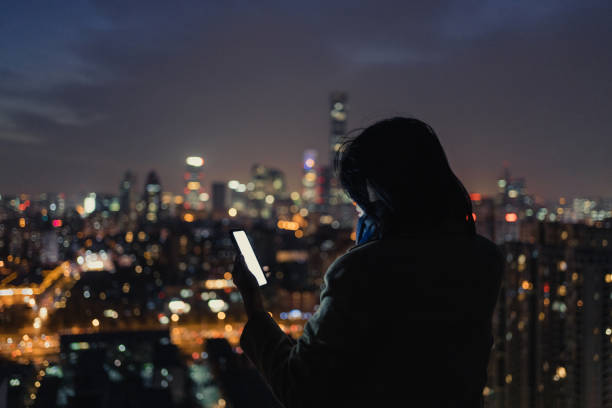 istock Woman Using Smartphone on Skyscraper Roof at Night 1307598737