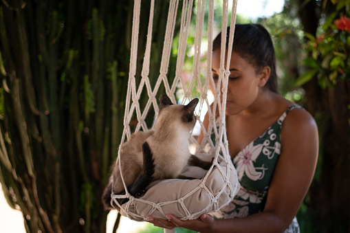Young woman with her siamese cat looking on a handmade macrame cat bed.