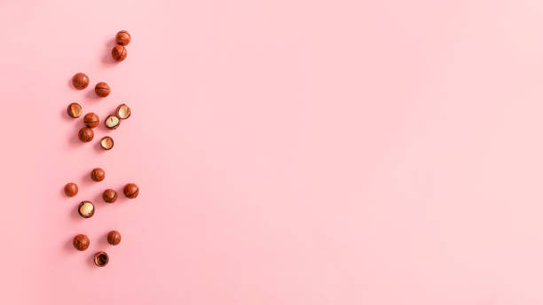 nueces de macadamia agrietadas sobre fondo rosa con espacio de copia - unshelled fotografías e imágenes de stock