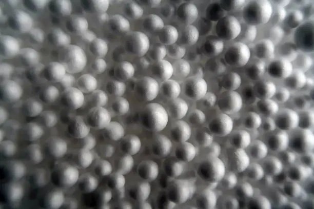 Large number of small grey white polystyrene or Styrofoam balls in plastic sack. Strong shadows. Metaphor for a full chaotic crowded space. Abstract textured background.