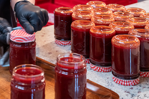 Woman filling strawberry jam into jars.