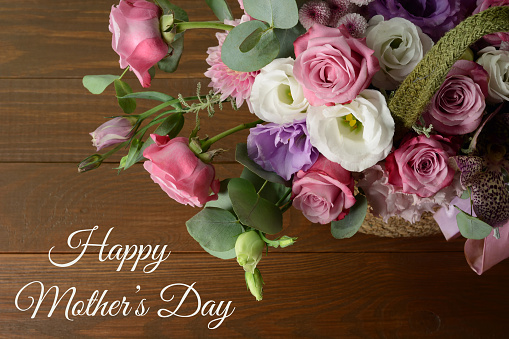Mothers day card. Bouquet of pink roses in basket and greeting text on wooden background closeup