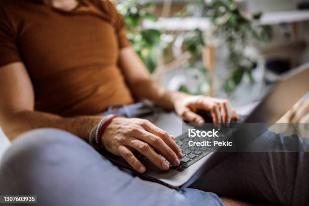 Unrecognisable Man Using His Laptop While Sitting On His Bed Stock Photo - Download Image Now