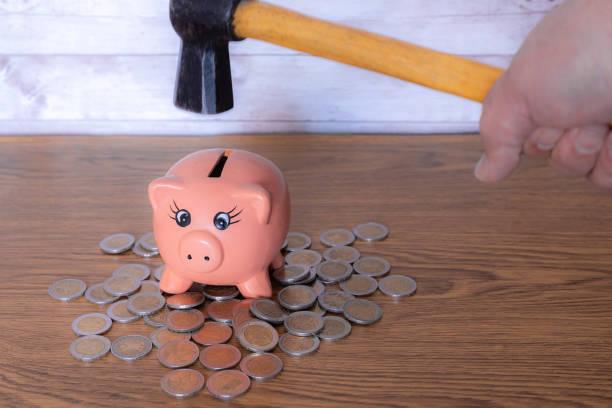 istock hand holding a hammer to break a pink ceramic piggy into which coins are inserted to save money in times of crisis economic concept 1307608107