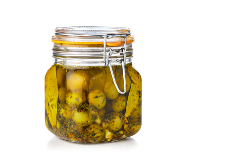 Marinated green olives in a glass jar isolated on white background. The composition is at the left of an horizontal frame leaving useful copy space for text and/or logo at the right. High resolution 42Mp studio digital capture taken with SONY A7rII and Zeiss Batis 40mm F2.0 CF lens