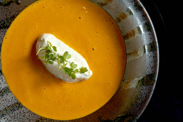 Lobster cream soup with cream cheese in a black bowl isolated on a black background. Restaurant food. Yellow cream soup stock photo
