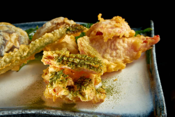 istock Vegetables fried in tempura, served in a white plate. Deep-fried asparagus, broccoli and mushrooms. Isolated over black background. Street food 1307610585