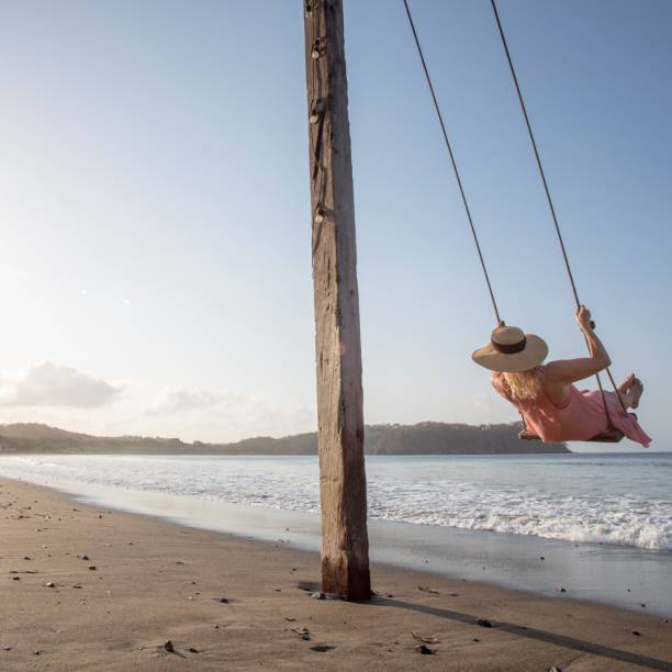 istock Woman enjoys waterfront swing on beach at sunrise 1307612370