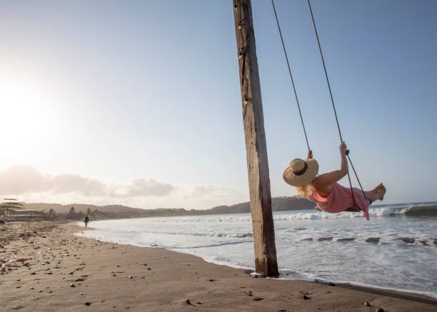 istock Woman enjoys waterfront swing on beach at sunrise 1307612380