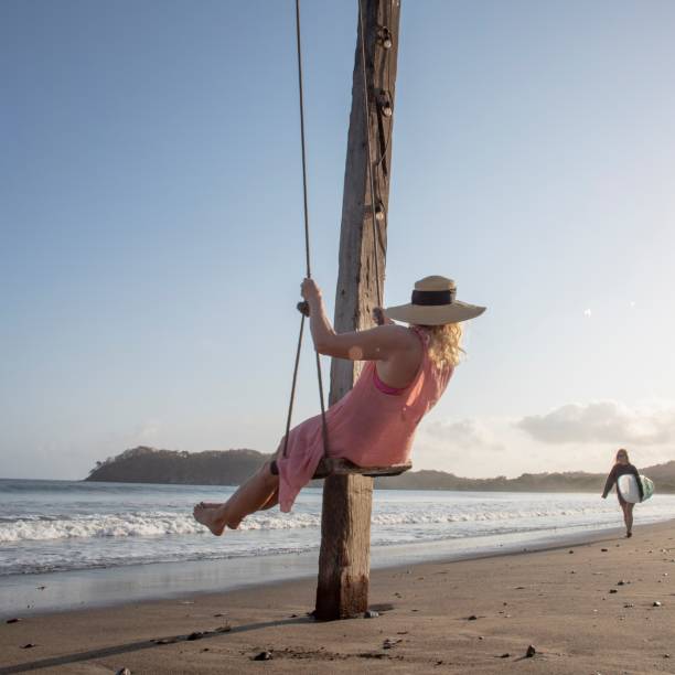 istock Woman enjoys waterfront swing on beach at sunrise 1307612412