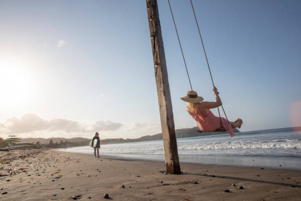 istock Woman enjoys waterfront swing on beach at sunrise 1307612434