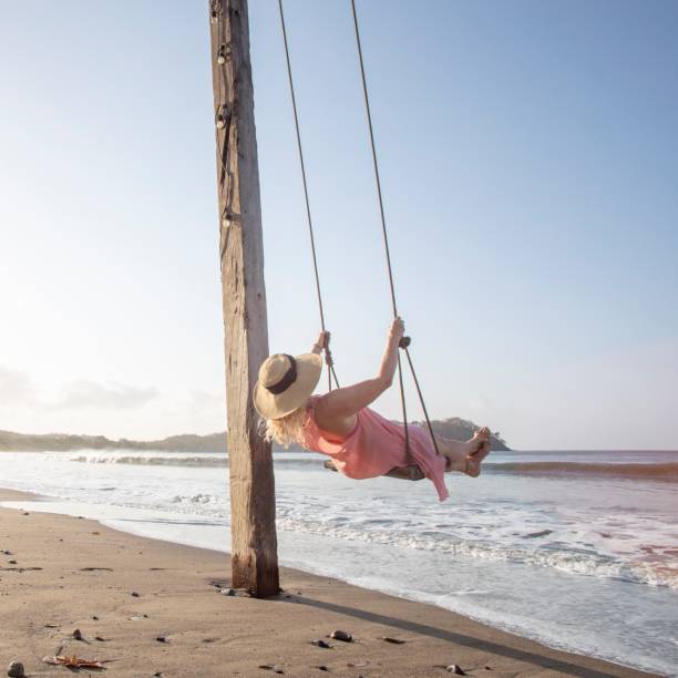 istock Woman enjoys waterfront swing on beach at sunrise 1307612466