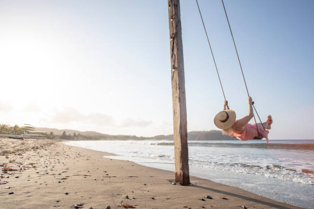 istock Woman enjoys waterfront swing on beach at sunrise 1307612482
