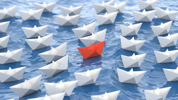 Leadership concept, red leader boat, standing out from the crowd of white boats, in the waves of the sea stock photo