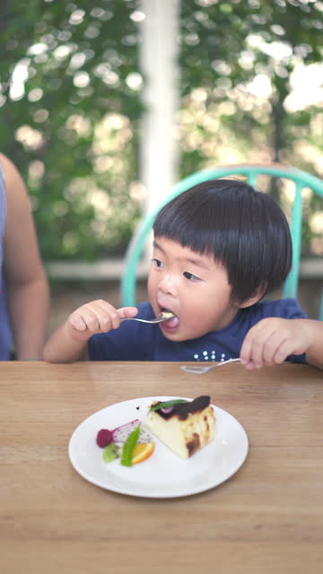 A vertical shot of an Asian baby boy eating Cheesecake with Mother at the restaurant