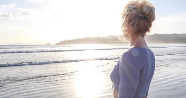 istock Young woman walks down sandy beach at sunrise 1307616381