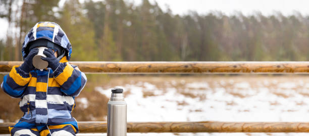 istock Young boy drinks hot beverage from a cup in a cold raini day. Resting, taking a break during hiking. Healthy living concept. Banner with copy space. 1307616413