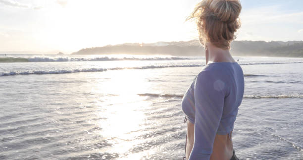 istock Young woman walks down sandy beach at sunrise 1307616515