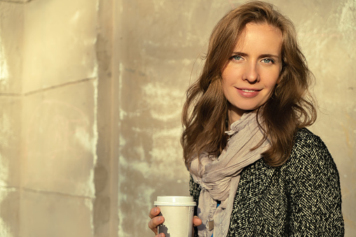 Close-up portrait of modern fashion elegantly beautiful woman with a cup of coffee in hand on the background of a gray textured wall.