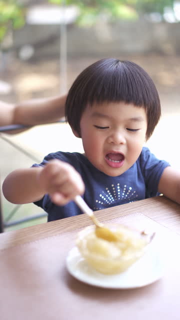 A vertical shot of an Asian baby boy eating dessert with Mother at the restaurant