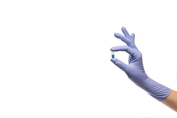 main dans le gant de latex avec une pillule dans une capsule sur un fond blanc - surgical glove human hand holding capsule photos et images de collection