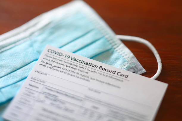 COVID-19 Vaccination Record Card A blank COVID-19 vaccination record card rests on top of a protective face mask. Photographed with a very shallow depth of field. immunization certificate photos stock pictures, royalty-free photos & images