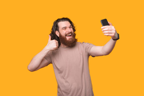 istock Amazed young bearded man taking selfie with smartphone and showing thumb up 1307625183