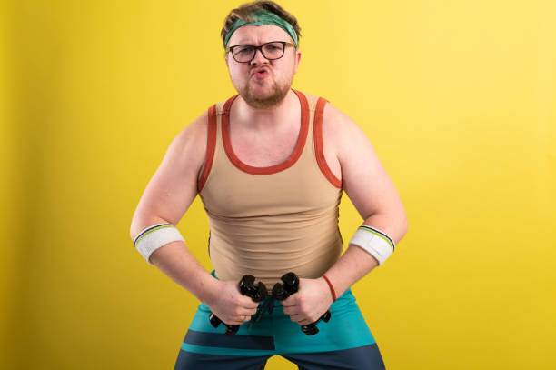 istock funny fat man doing exercises with dumbbells. Overweight. yellow background 1307625741