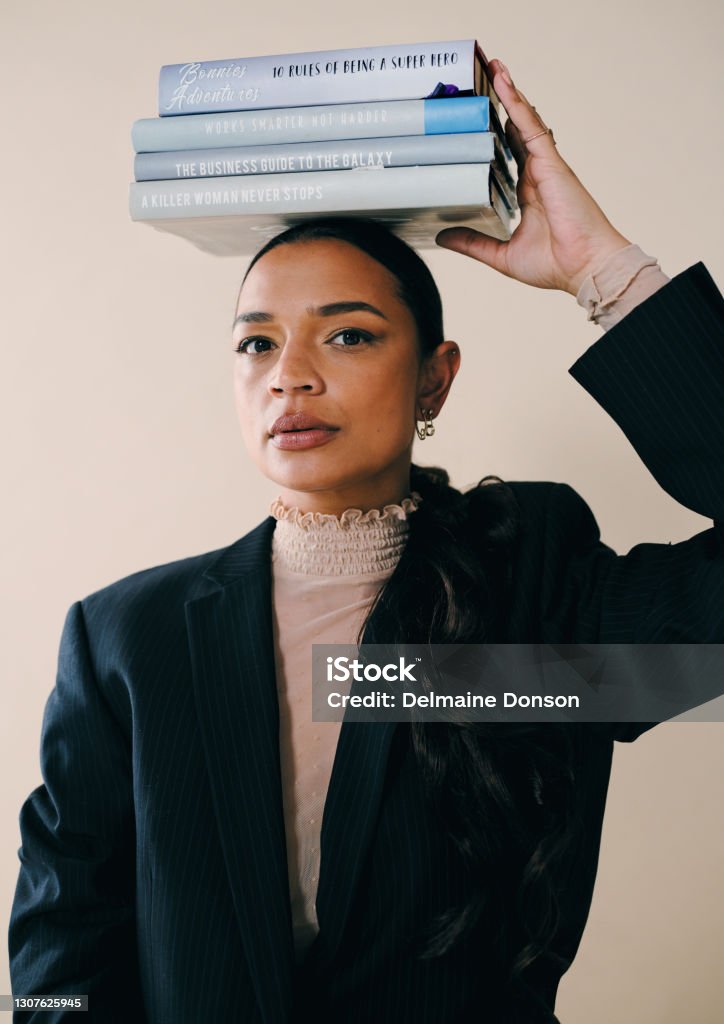 Sweet, smart and here to slay Studio portrait of a beautiful young woman balancing a pile of books on her head against a brown background Abstract Stock Photo